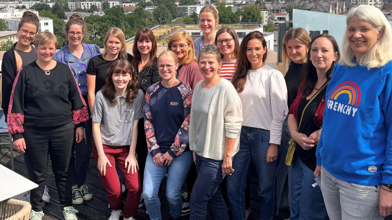 Mitglieder von Female Voice und Workshopleiterin Astrid Eckstein stehen auf einem Rooftop mit der Frankfurter Skyline im Hintergrund